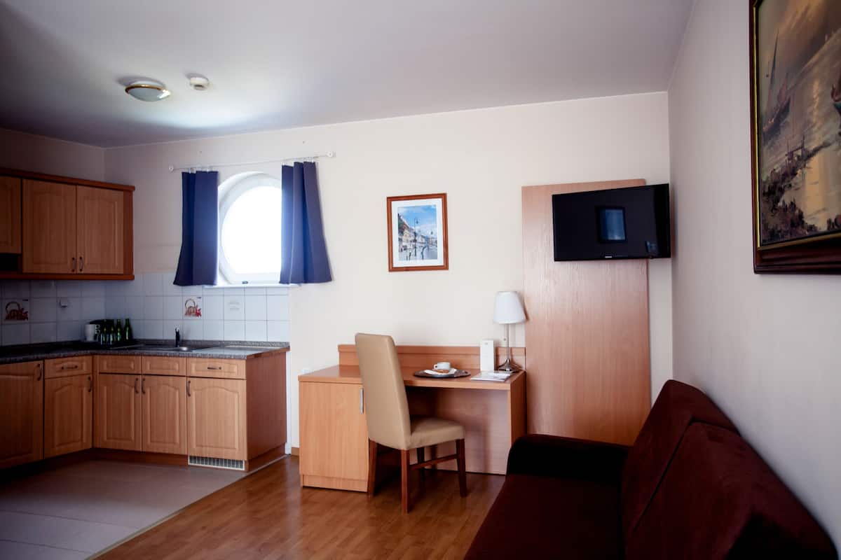 Uma cozinha compacta com armários de madeira, um espaço de refeições com mesa e cadeira, uma TV fixada na parede e uma janela com cortinas.