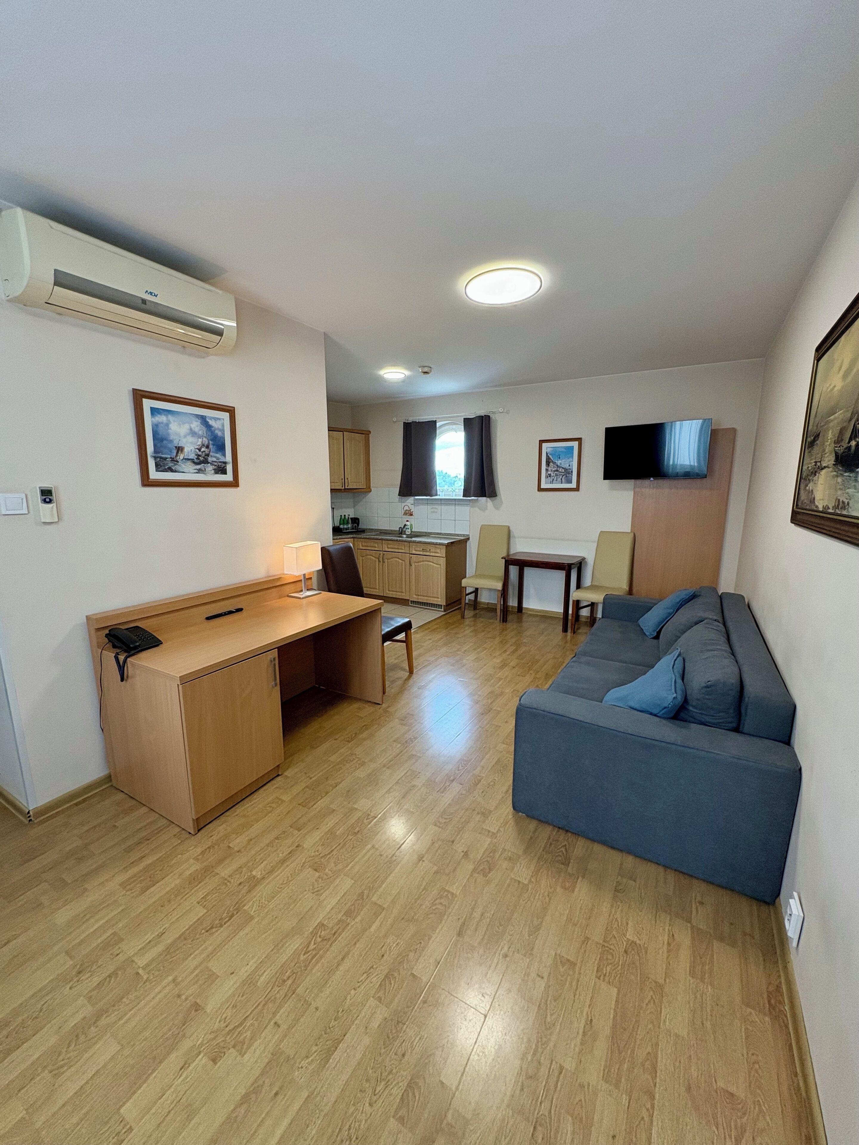 A compact living space with a kitchenette, a sofa, a desk, and a TV mounted on the wall.