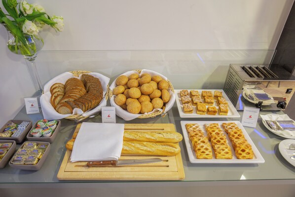 A buffet with various breads, pastries, and cheese platters.