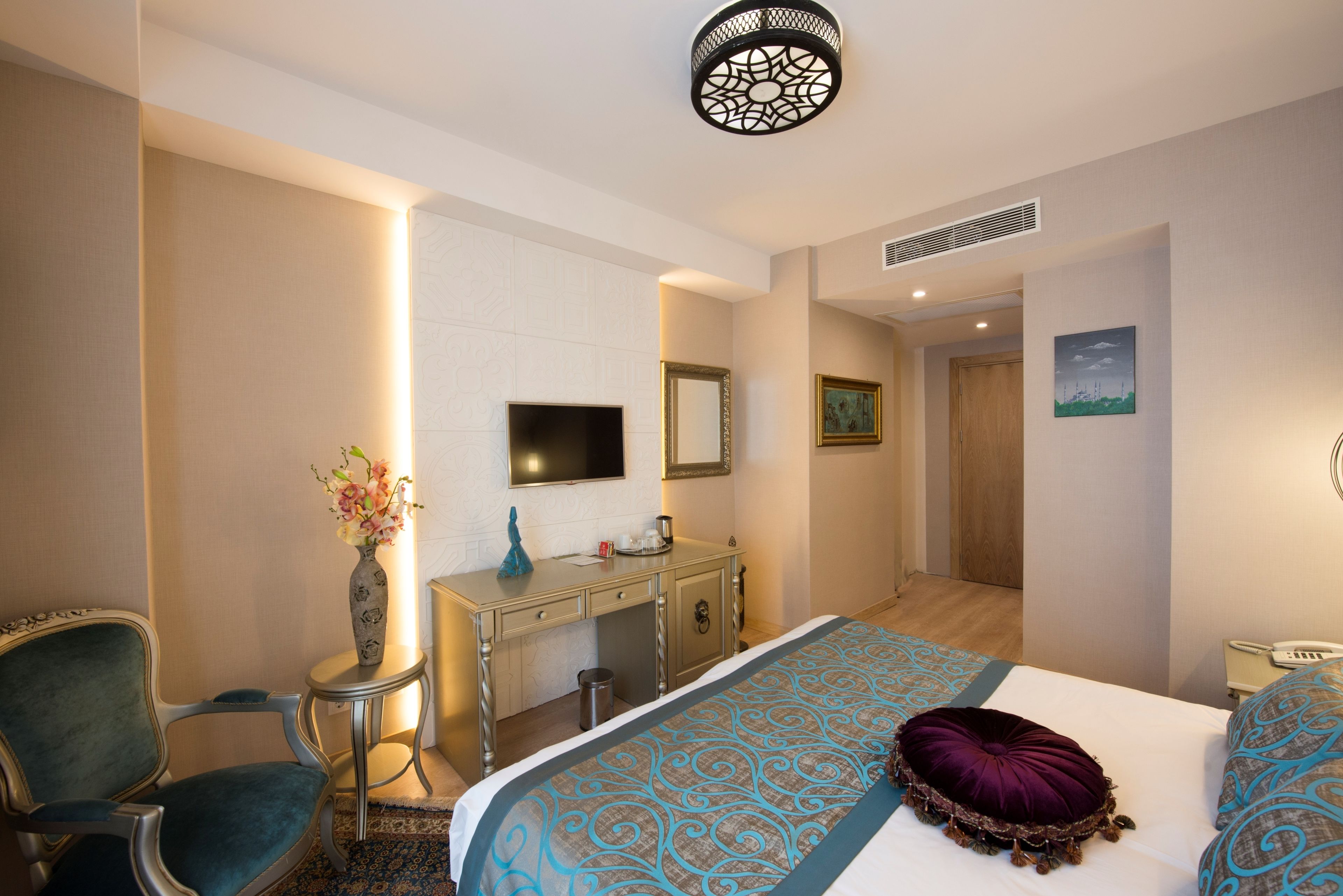 Habitación de hotel con cama, escritorio, silla, televisión, espejo y un cuadro en la pared.