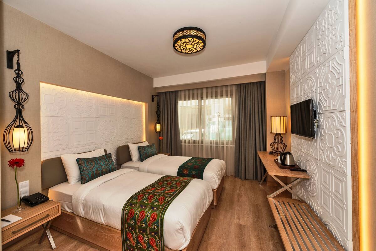 A hotel room with two beds, a desk, a TV, and a decorative wall.