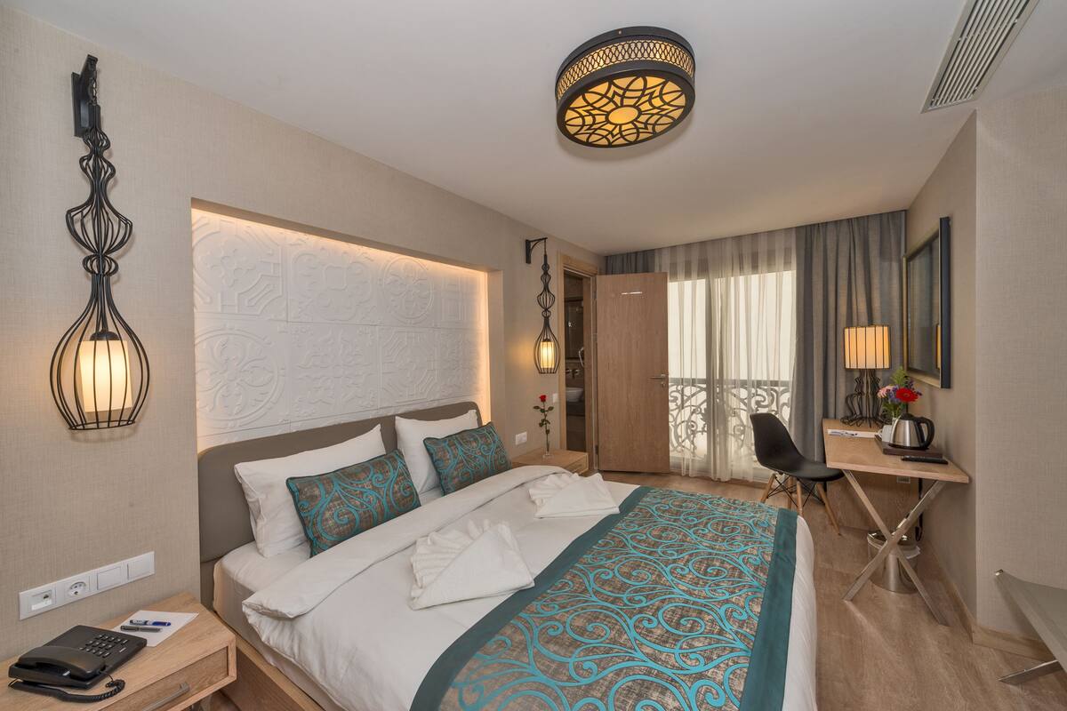 A hotel room with a bed, a desk, a chair, a lamp, and a decorative wall piece.