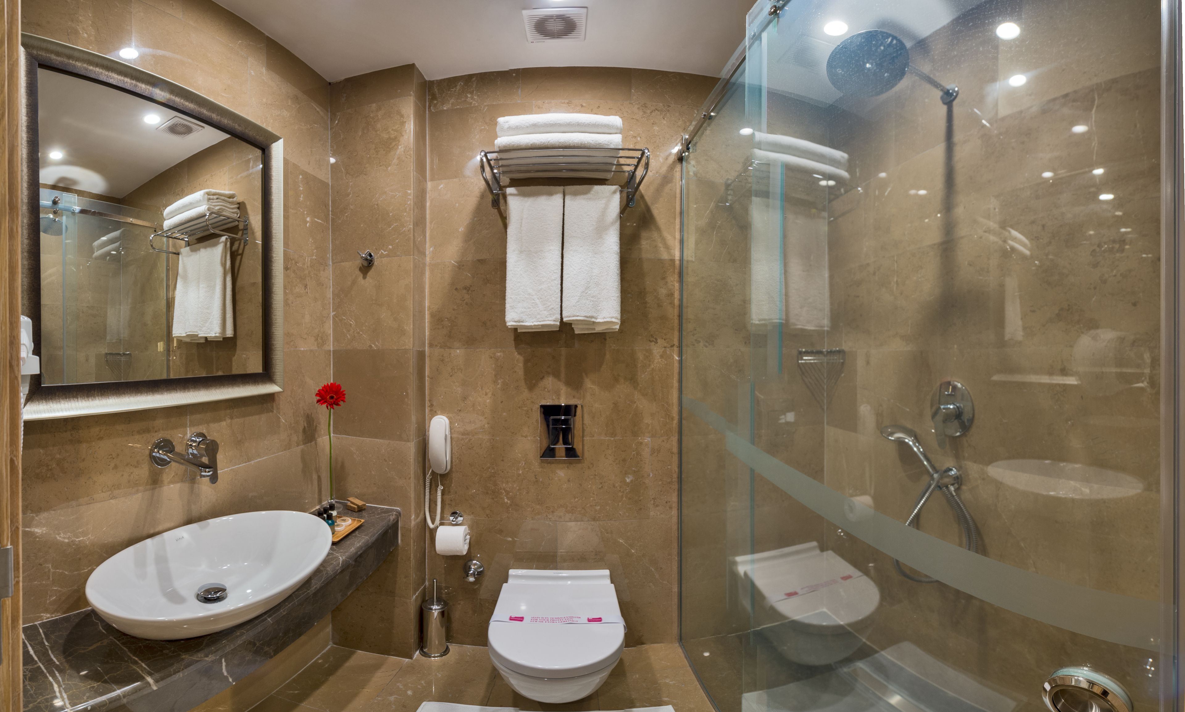 Un baño moderno con un espejo grande, un lavabo, un inodoro y una zona de ducha con mampara de vidrio.