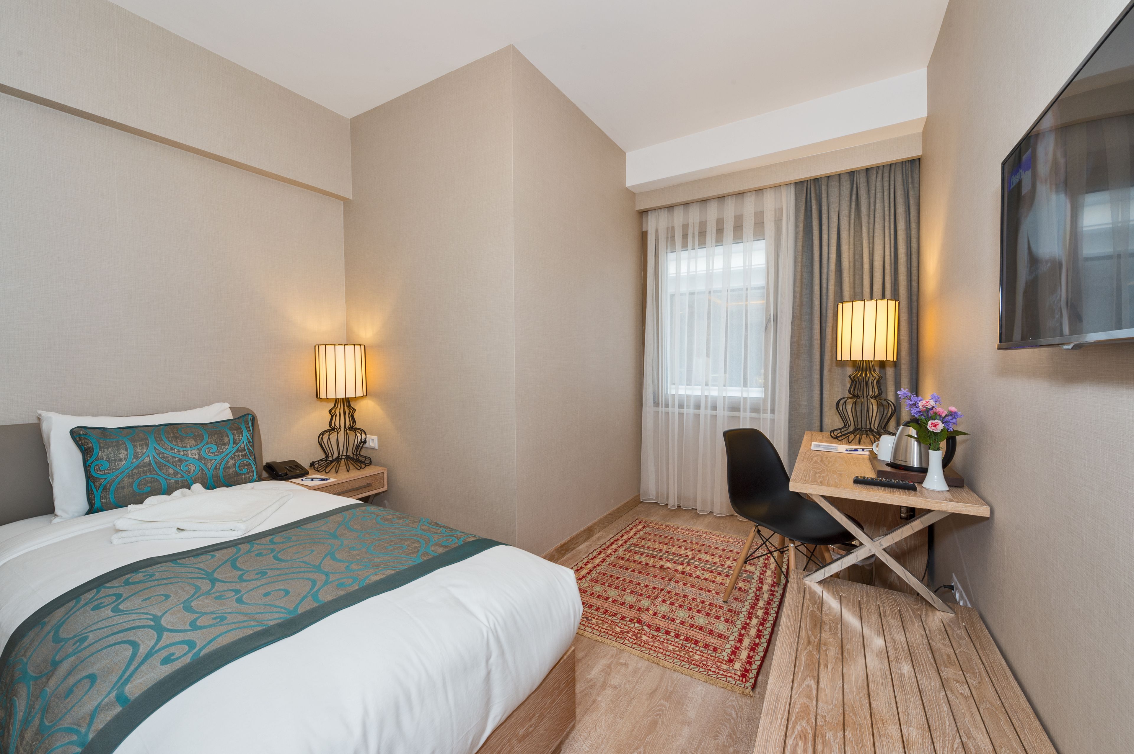Une chambre d’hôtel avec un lit, un bureau, une chaise, une télévision et une fenêtre avec des rideaux.