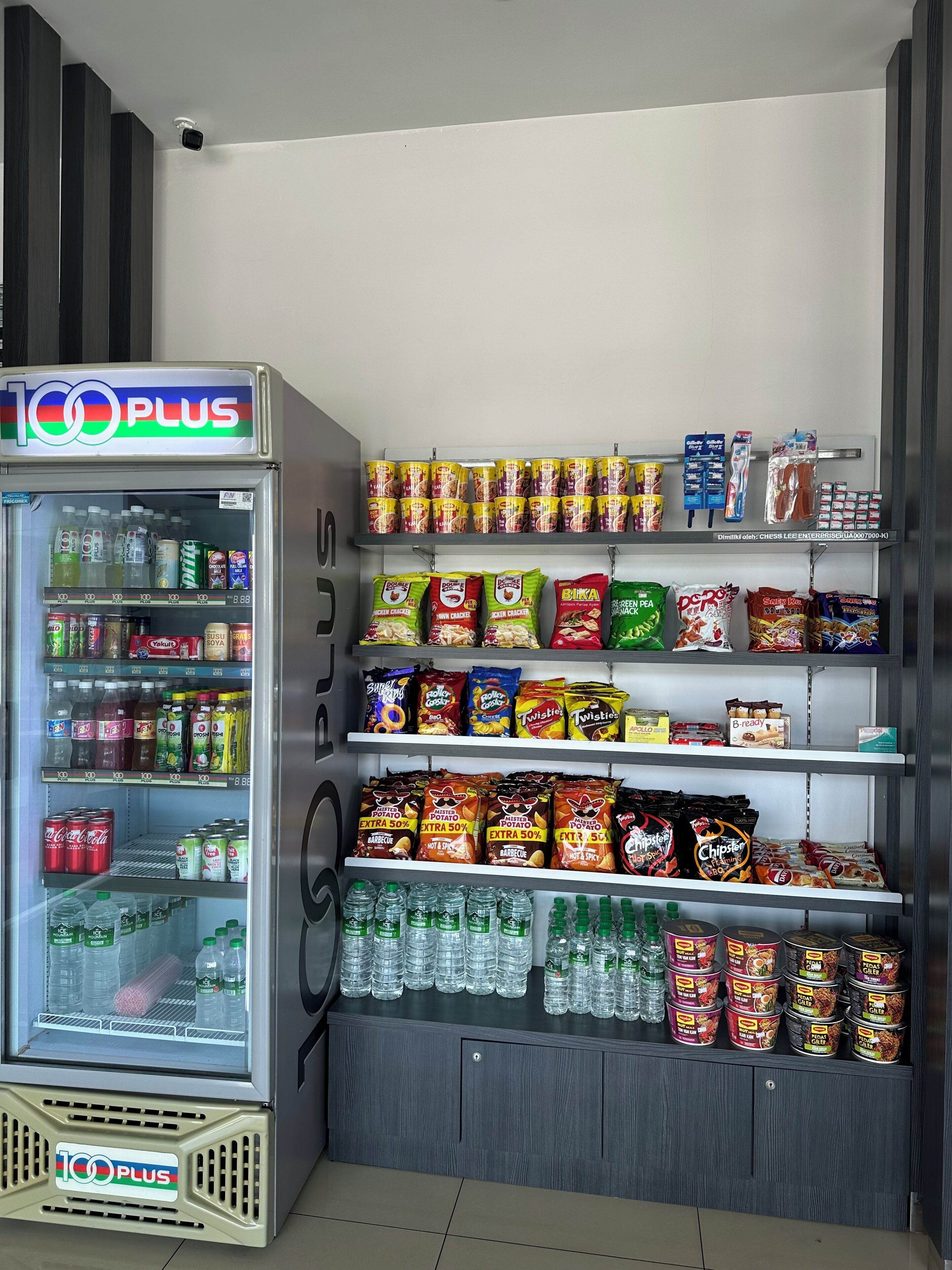 Een 100 PLUS automaat met diverse drankjes en snacks, waaronder blikjes, flessen en verpakte producten.