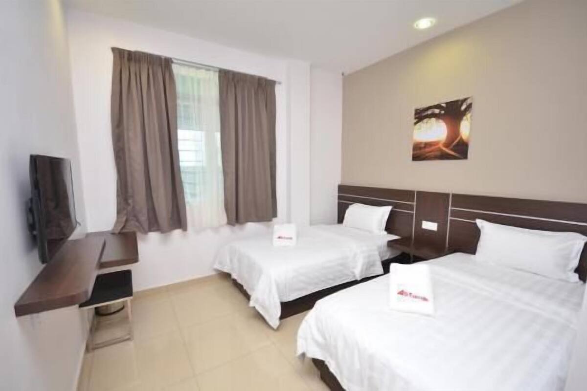 A hotel room with two beds, a TV, and a window with curtains.