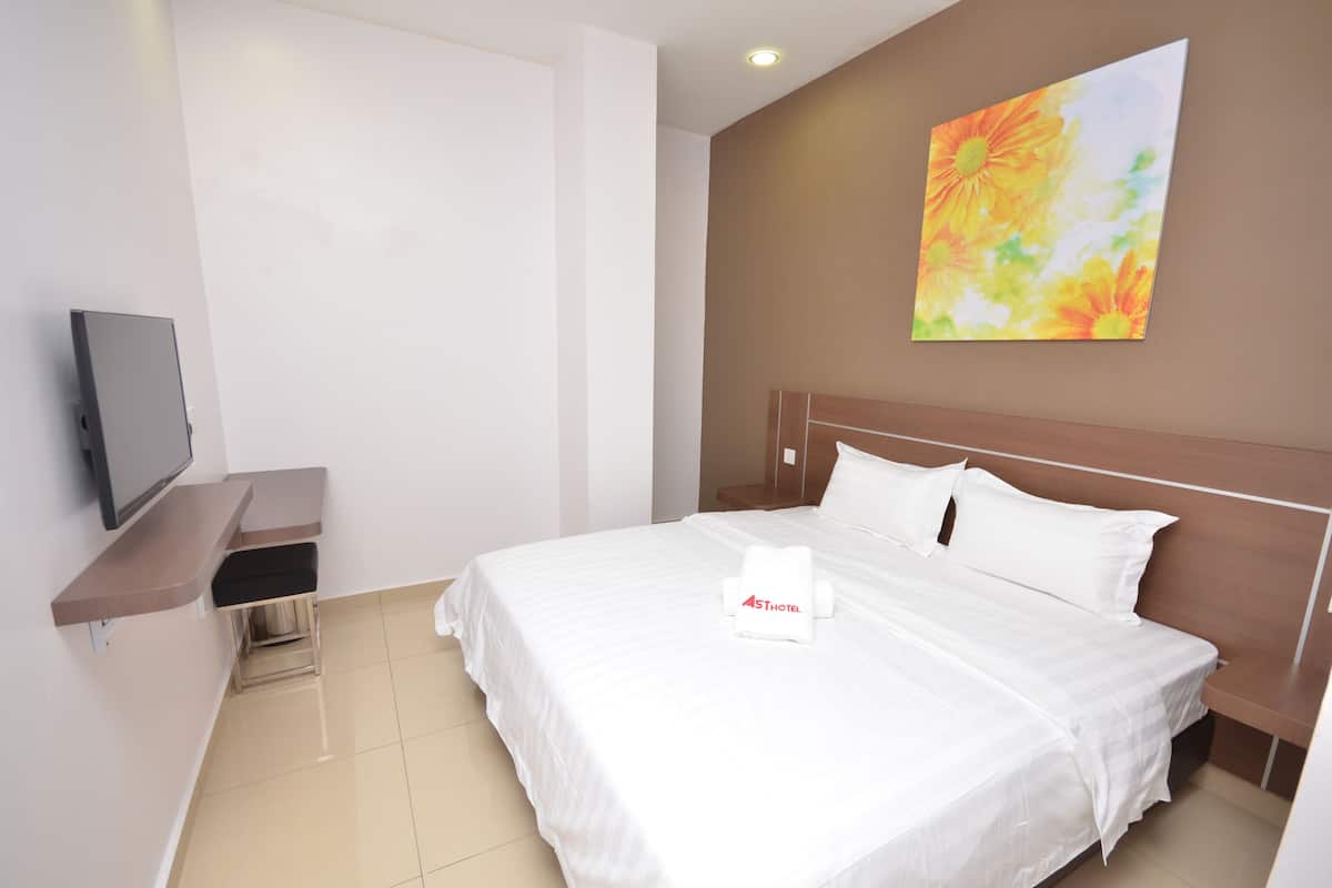 A hotel room with a bed, a TV on a stand, a painting on the wall, and a towel with a logo.