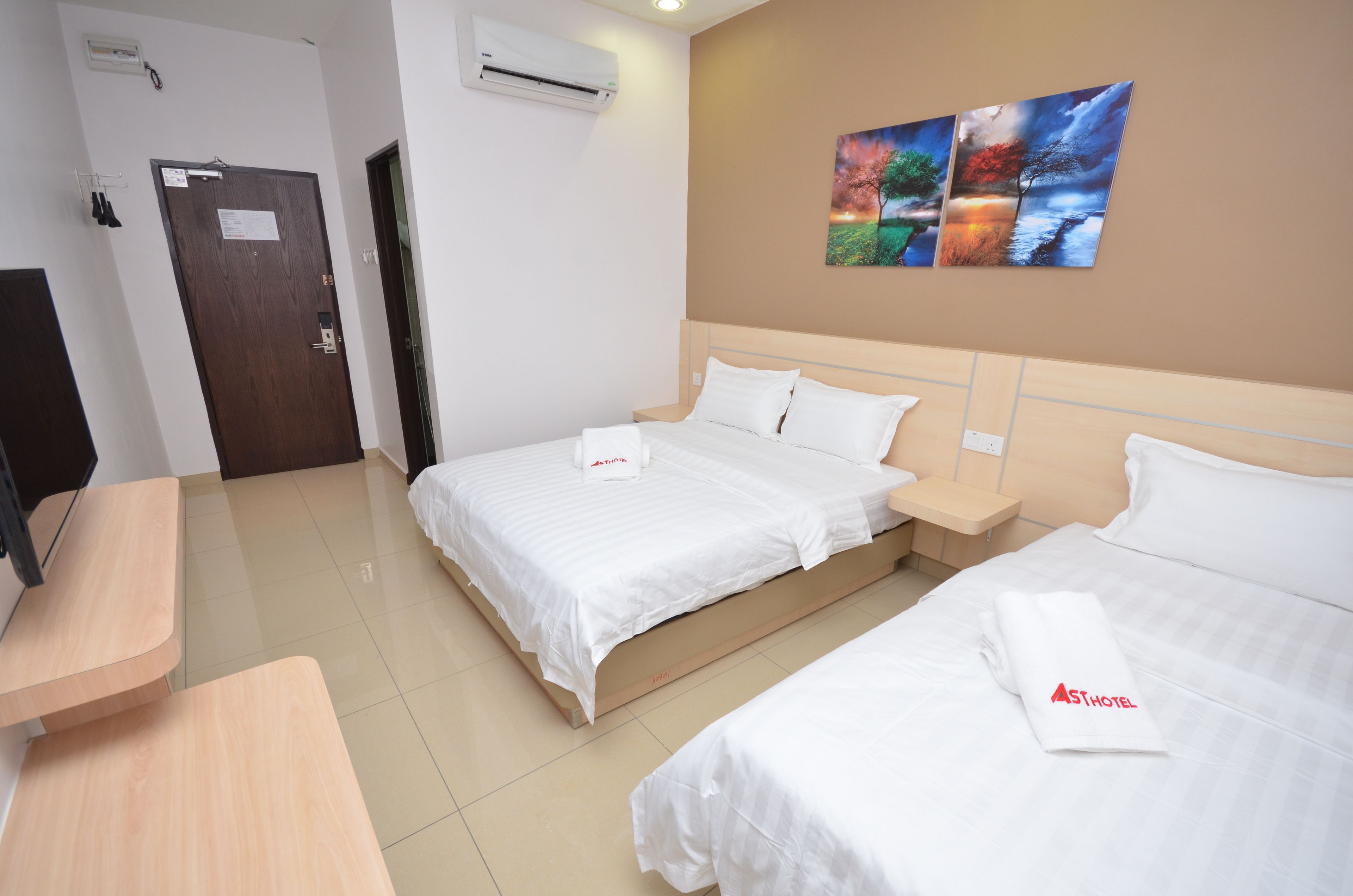 A hotel room with two beds, a wooden desk, and a wall-mounted air conditioner.