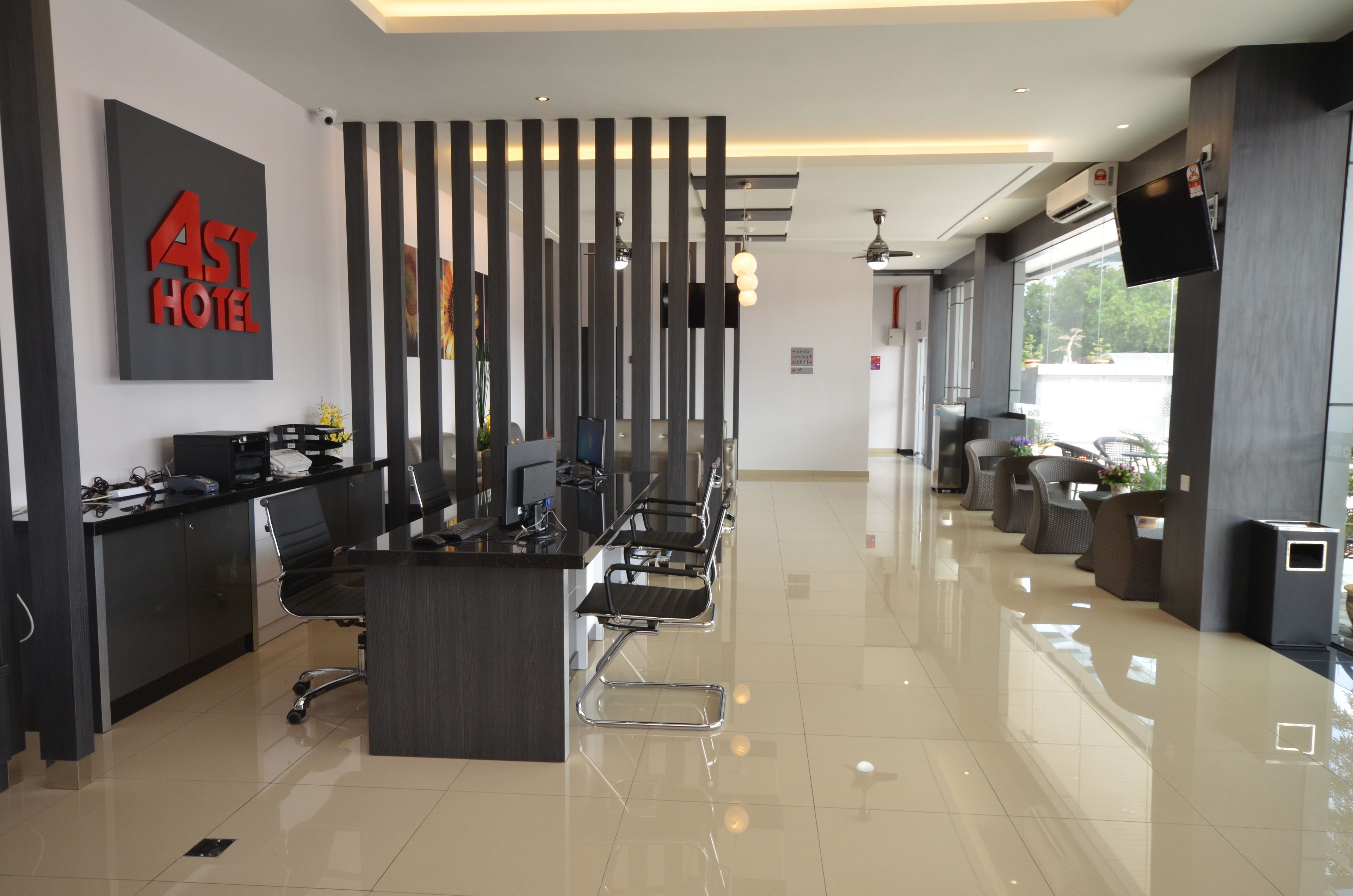 A modern hotel reception area with a reception desk, seating, and a large window providing a view of the outdoors.
