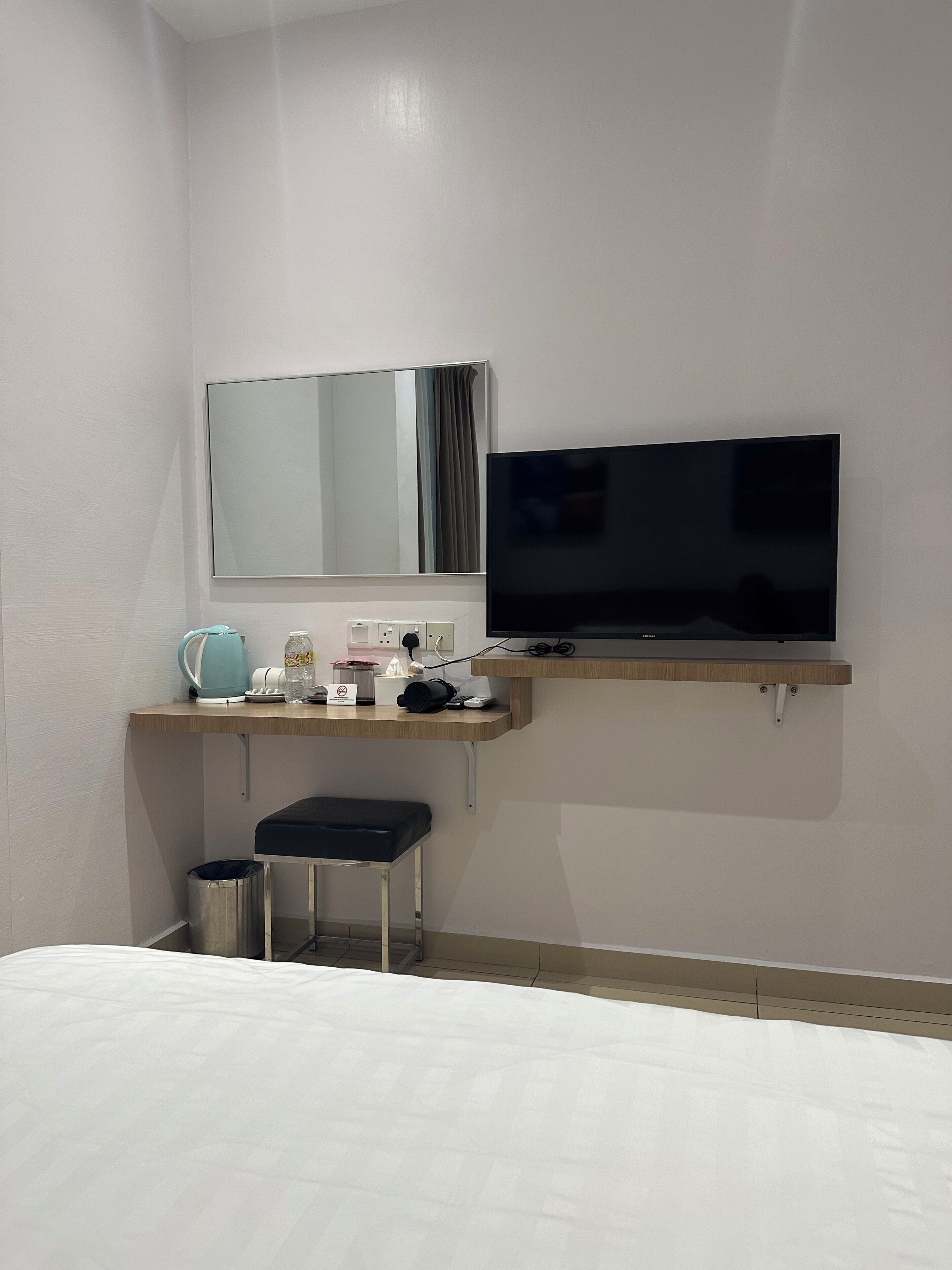Ein Hotelzimmer mit Bett, Schreibtisch, Flachbildfernseher, Spiegel und einem kleinen Papierkorb.