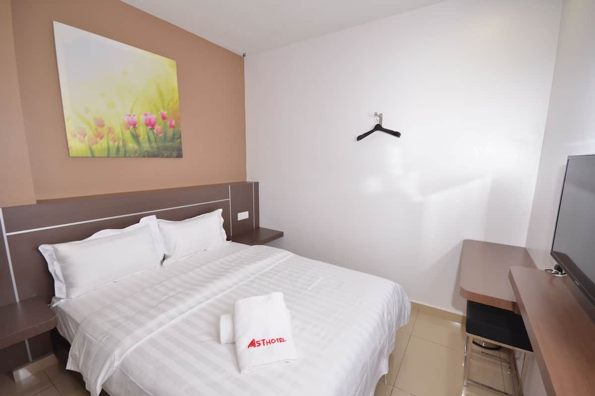 A hotel room with a bed, a painting on the wall, a TV, and a wooden desk.