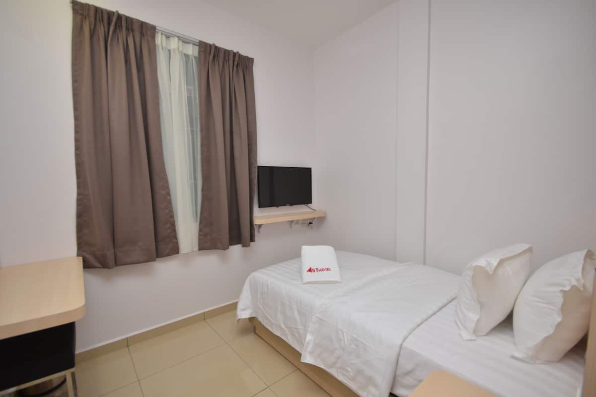 A hotel room with a bed, a TV on a shelf, a desk, and a window with curtains.