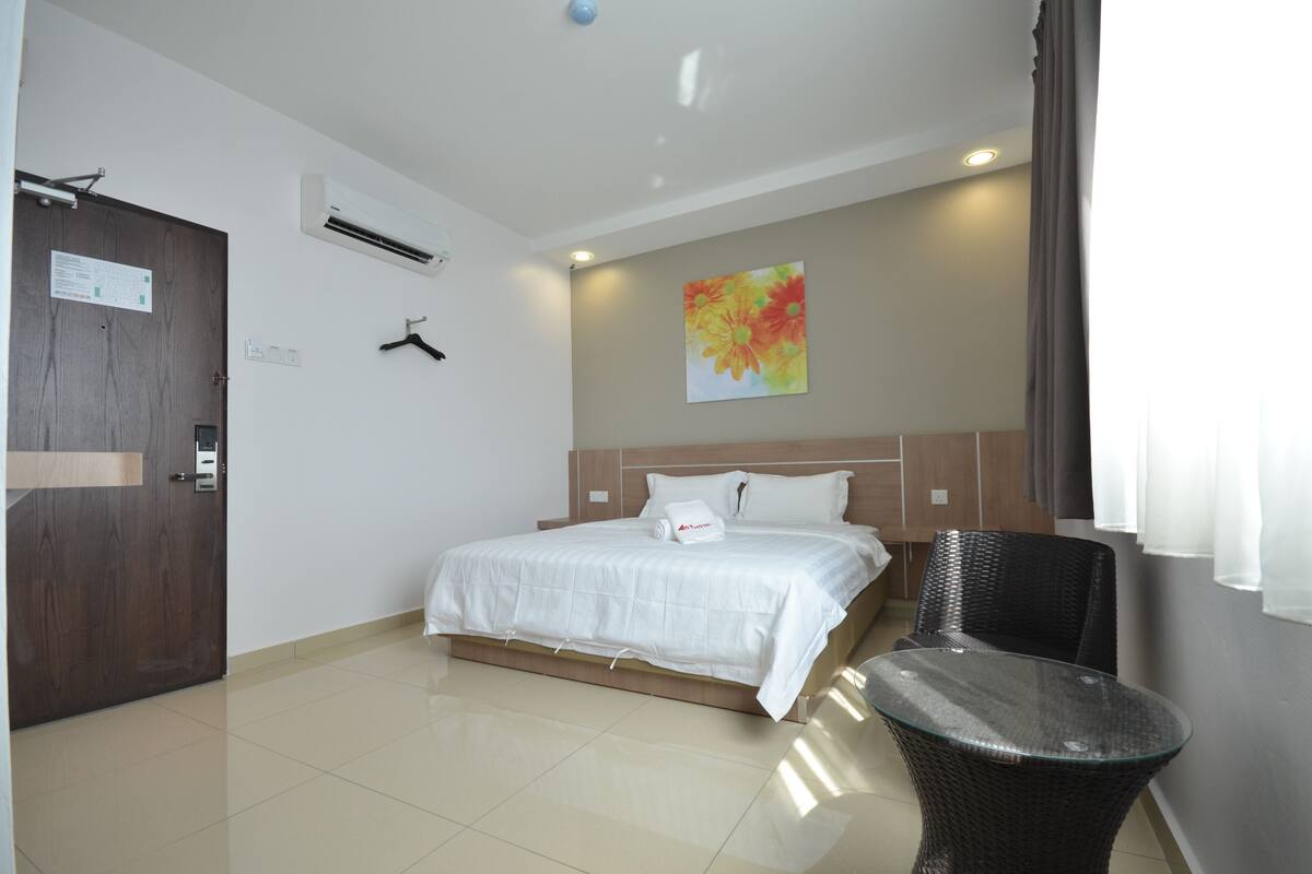 A hotel room with a bed, a chair, a wardrobe, and a painting on the wall.