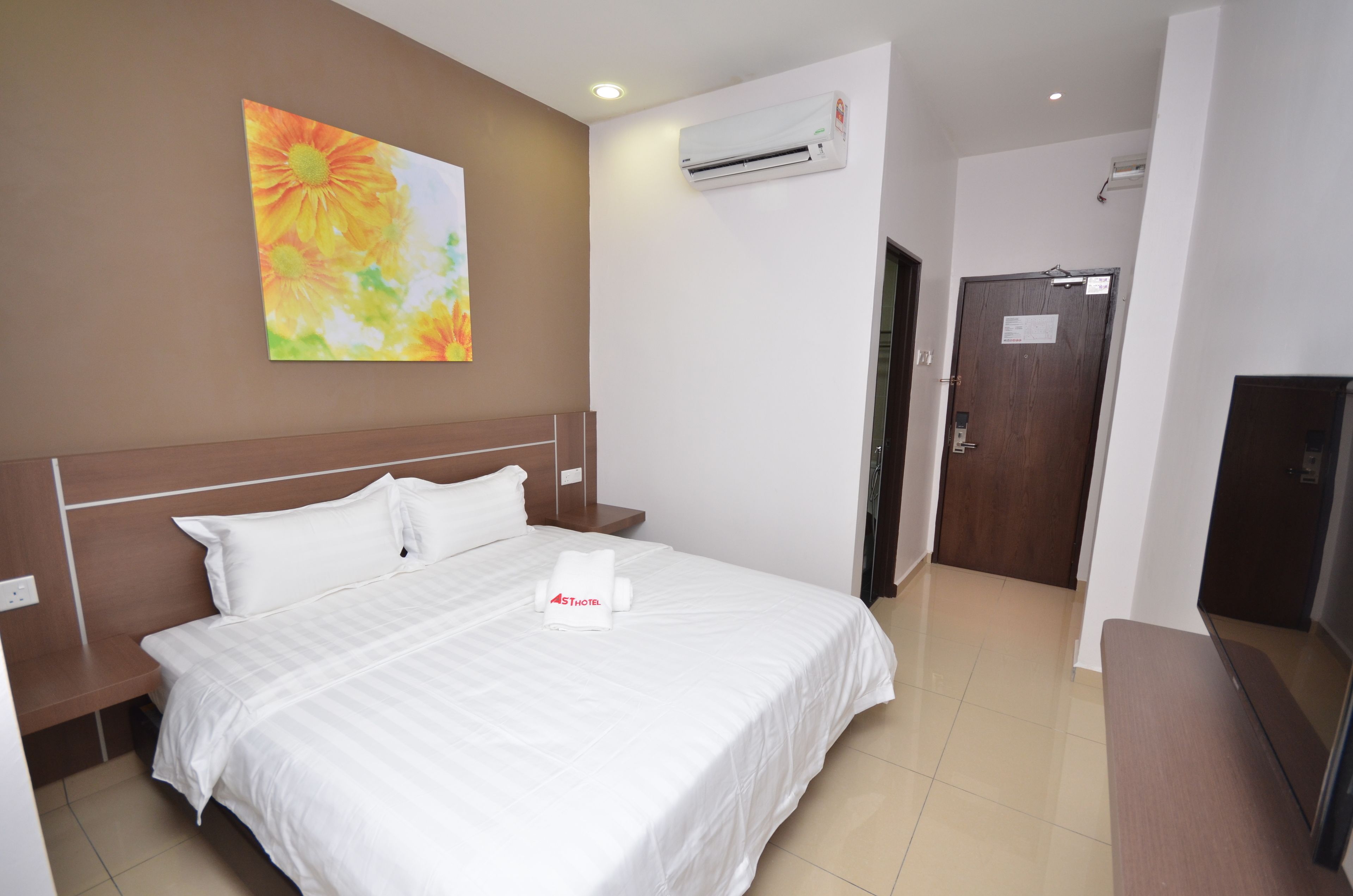 A hotel room with a large bed, a nightstand, a wall-mounted air conditioner, and a door with a sign.