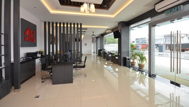 A modern hotel reception area with a reception desk, chairs, a chandelier, and a large window offering a view of the outside. - AST Hotel (Alor Setar)