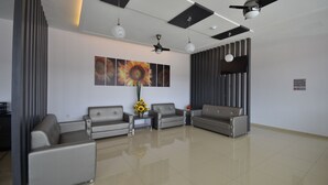 A spacious, modern waiting area with grey sofas, a large wall-mounted artwork, ceiling fans, and a clean, tiled floor. - AST Hotel (Alor Setar)