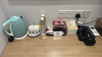 Una kitchenette con una tetera, tazas, una botella de agua, sobres de café, pañuelos de papel y un secador de pelo.