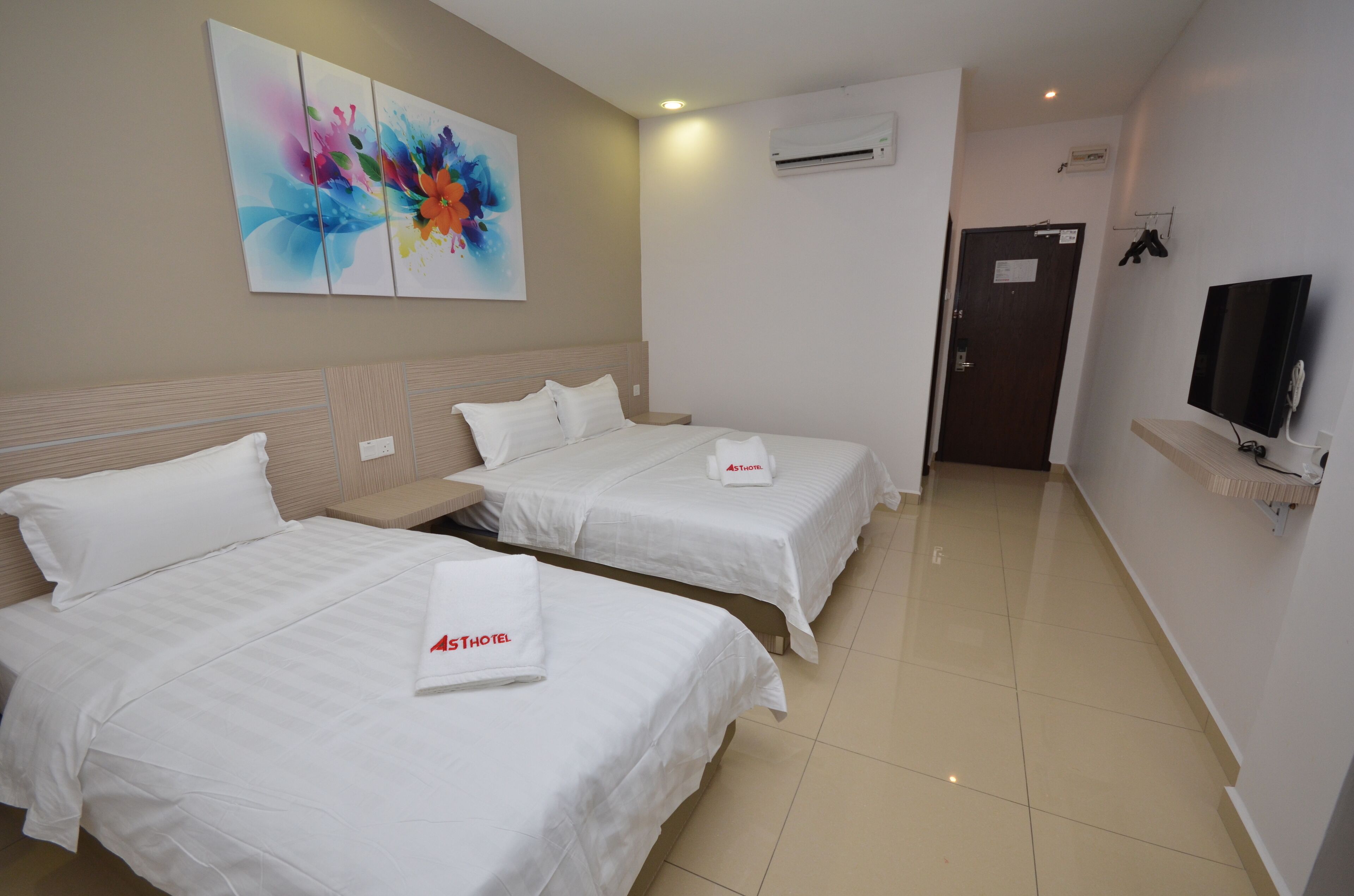 Quarto de hotel com duas camas, televisão, ar condicionado e um quadro abstrato colorido na parede.