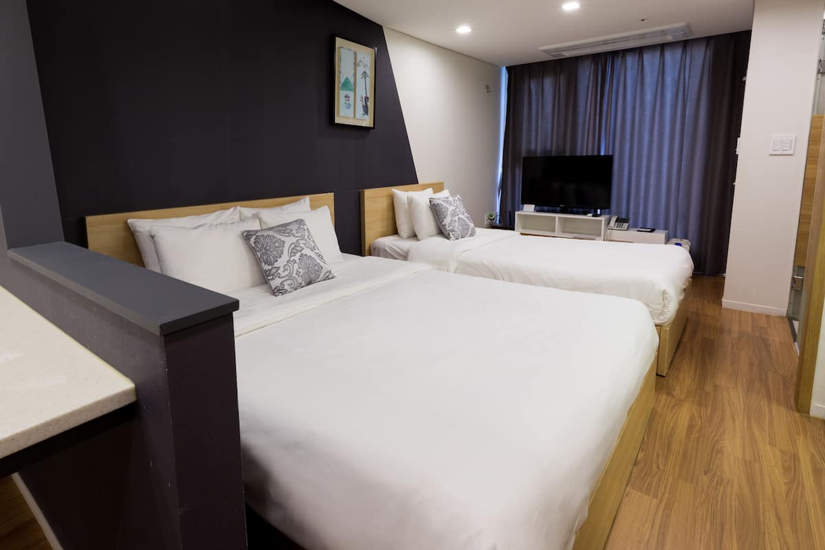 A hotel room with two beds, a flat-screen TV, a desk, and a large window with curtains.
