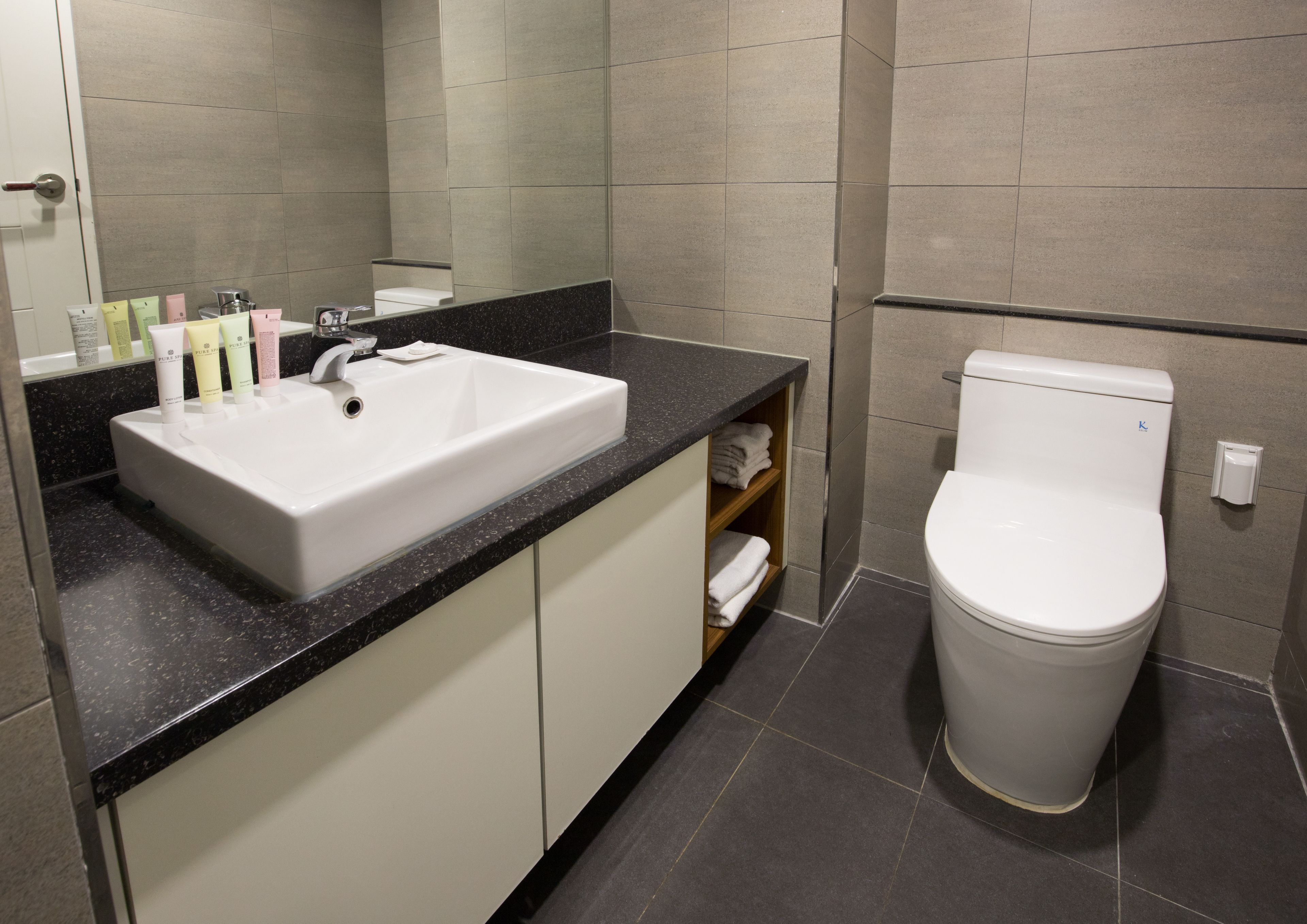 Un baño moderno con lavamanos blanco, encimera negra y retrete blanco.