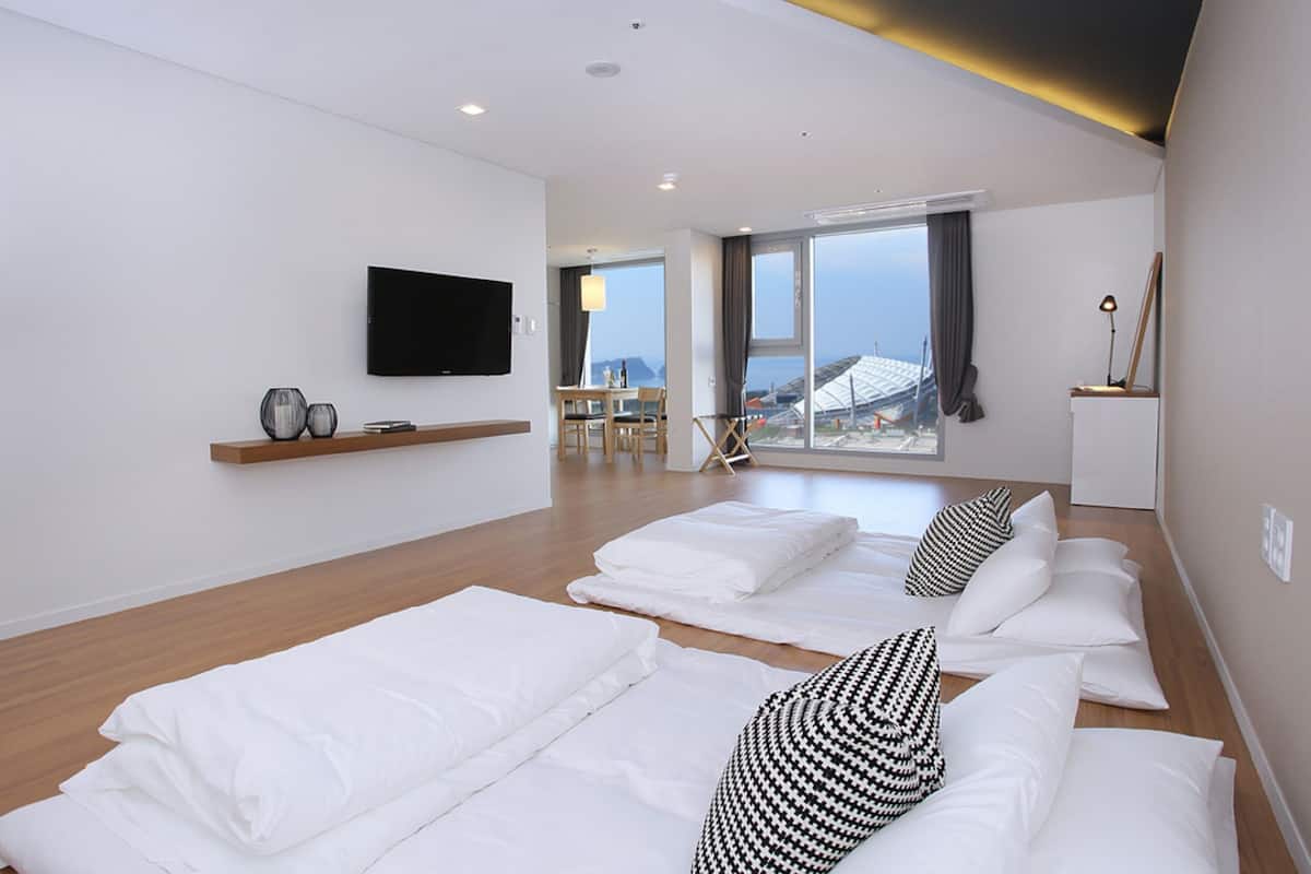 A hotel room with a large bed, a TV mounted on the wall, and a view of the city through large windows.
