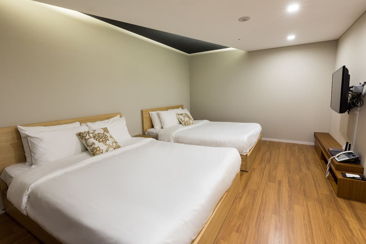 A hotel room with two beds, wooden flooring, a TV mounted on the wall, and a desk with a telephone.