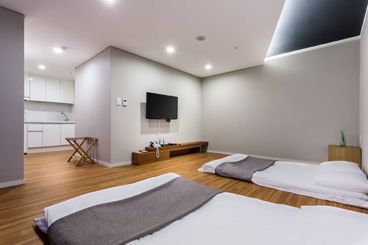 A modern hotel room with two beds, a TV, a small kitchenette, and a wooden floor.