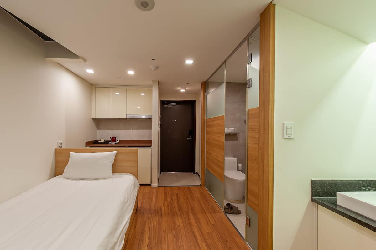 A compact hotel room with a bed, a small kitchenette, and a bathroom.