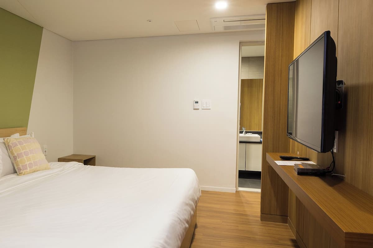 A hotel room with a bed, a television, and a wooden cabinet.