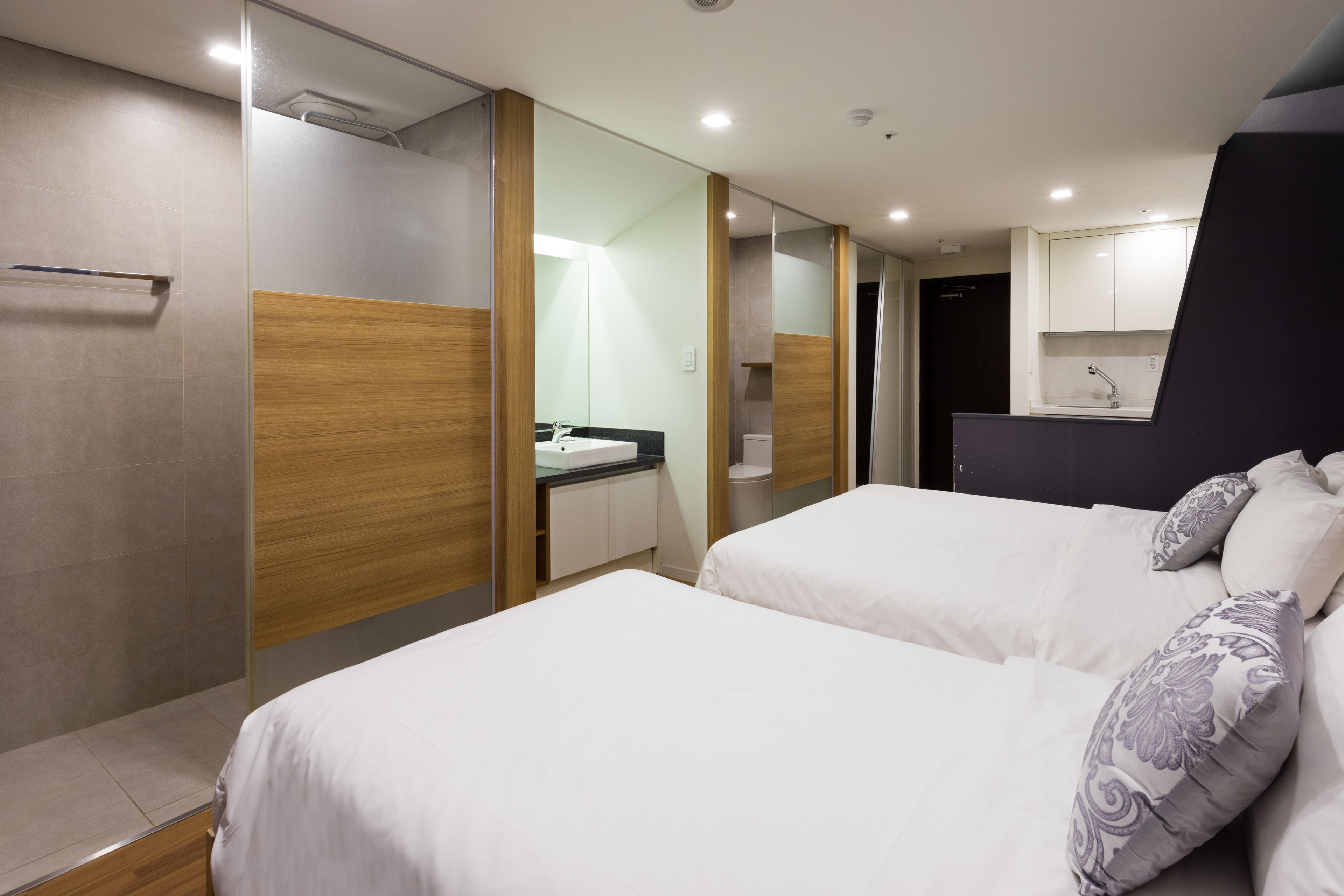 A modern hotel room with two beds, a bathroom, and a kitchenette.