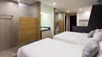 A modern hotel room with two beds, a bathroom, and a kitchenette.