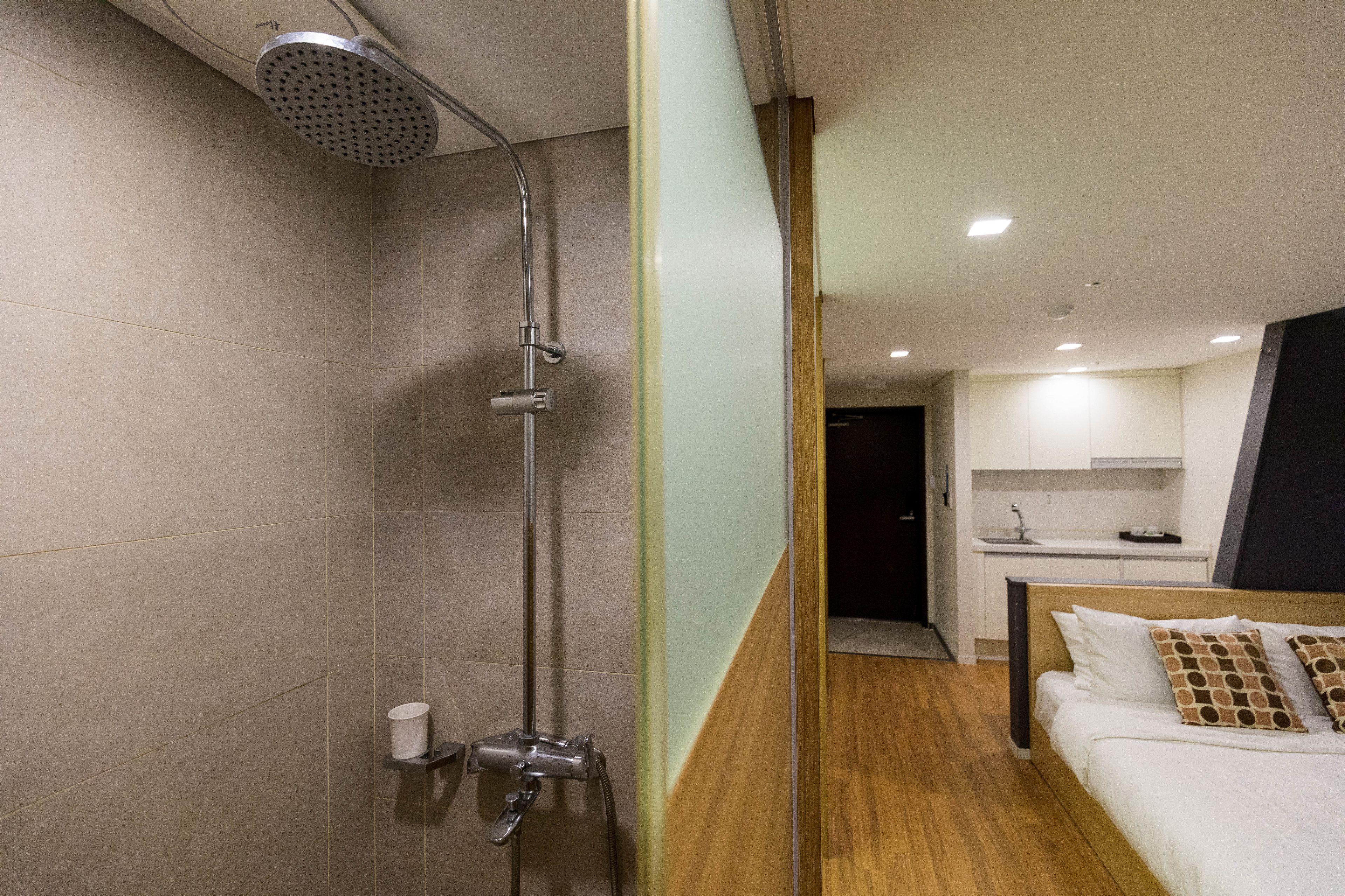A modern hotel room with a shower, a bed, and a kitchenette.