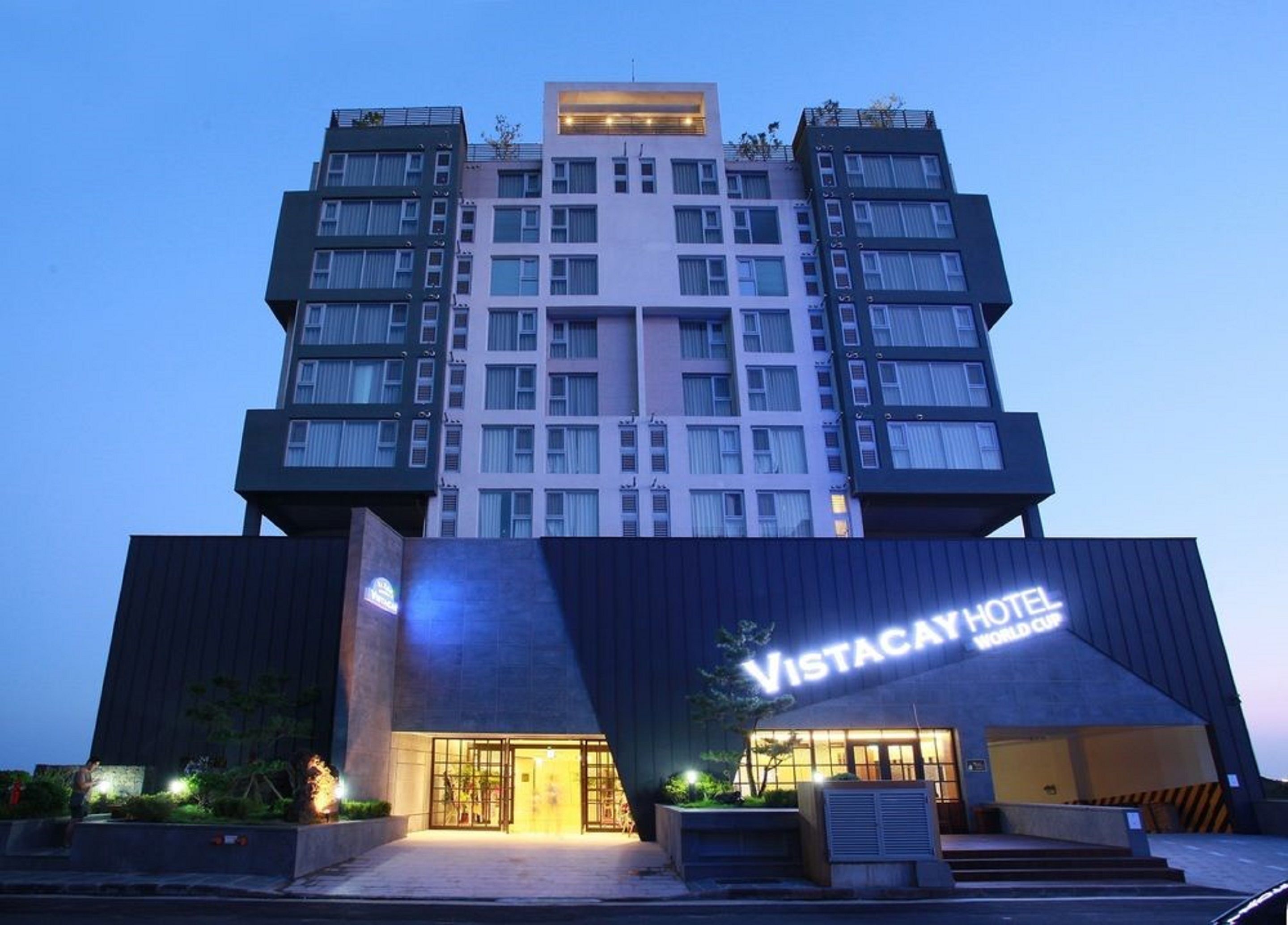 Un moderno edificio de hotel con una entrada destacada y un letrero que dice "Vistacay Hotel World Cup".