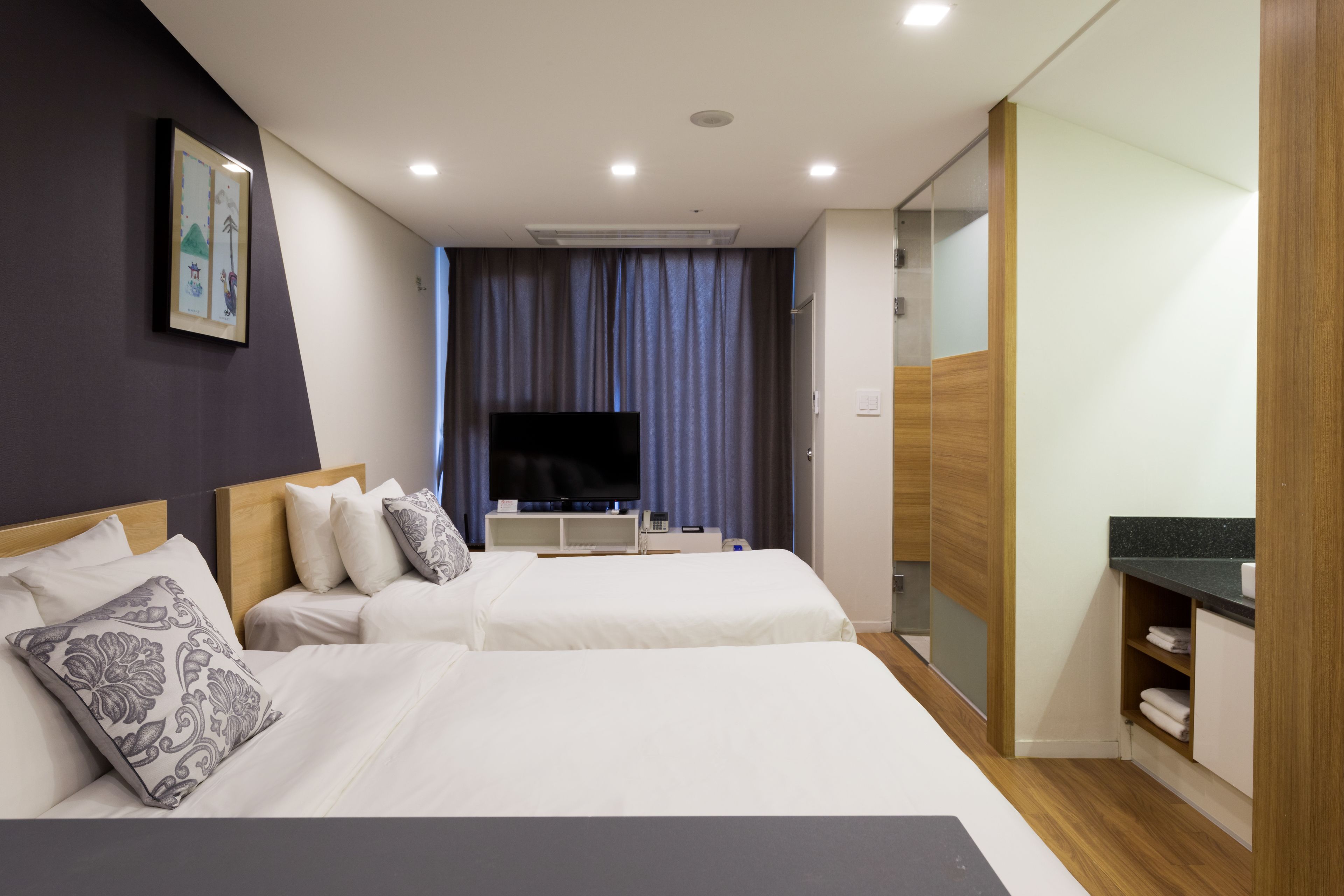 A hotel room with two beds, a flat-screen TV, a wooden wardrobe, and a bathroom with a mirror.