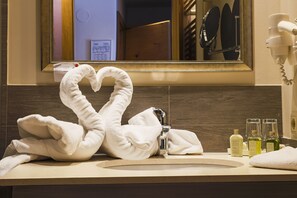 A bathroom with a heart-shaped towel arrangement, a sink, and toiletries.