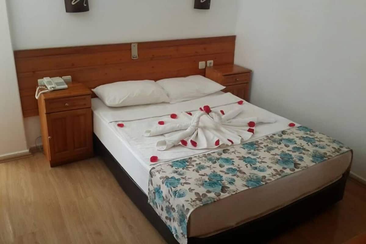 Cama bem arrumada com colcha floral, cabeceira de madeira, mesa de cabeceira com um telefone e dois interruptores de luz na parede.