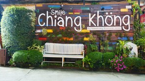 A wooden bench with a colorful wall behind it, featuring the text "Smile Chiang Khong" and "By Namkhong Riverside Hotel". - Namkhong Riverside Hotel Chiang Rai (Chiang Khong)