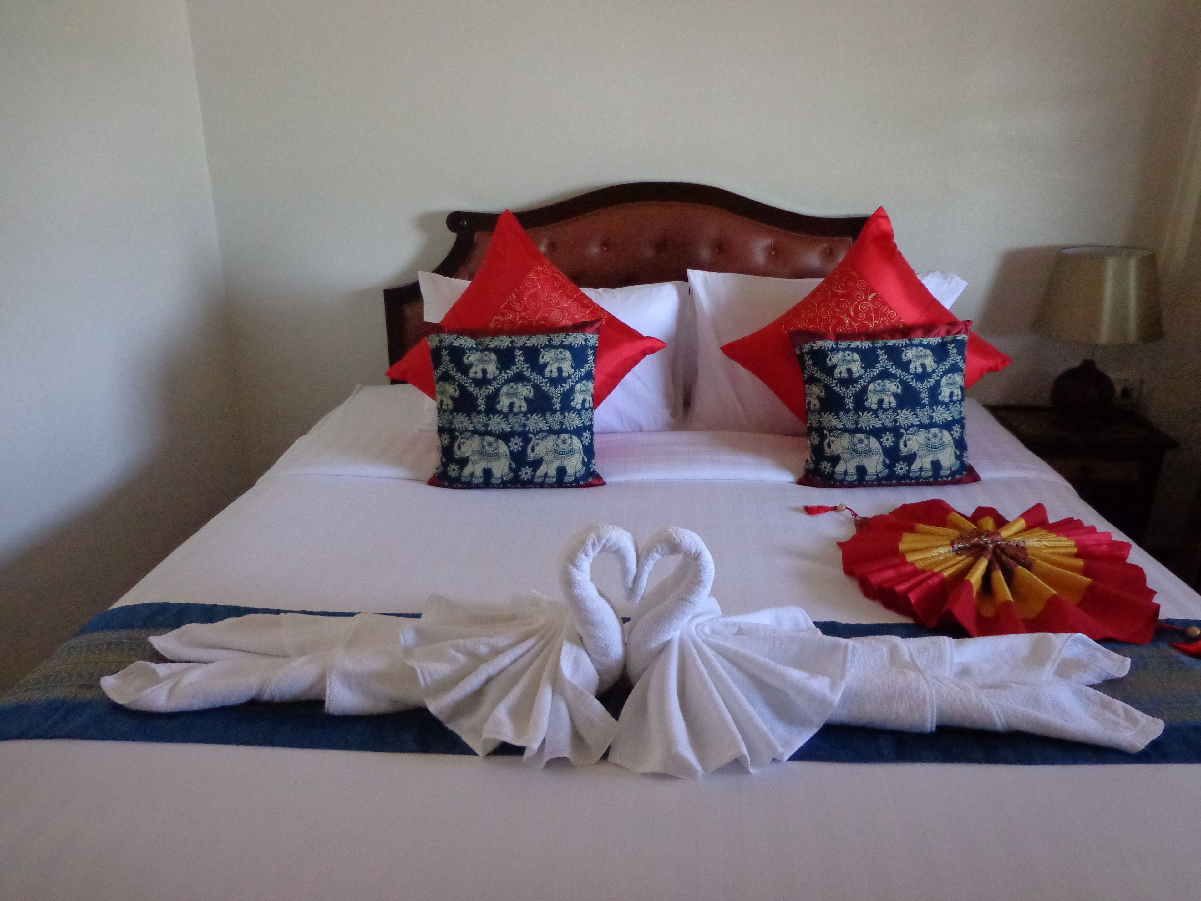 A neatly made bed with a blue and white striped bedspread, two decorative pillows with elephant patterns, and a red and gold decorative item on the bed.