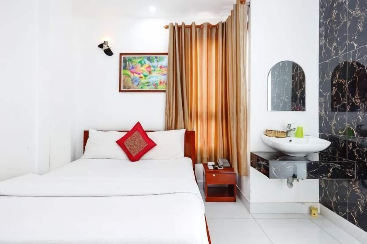 A hotel room with a bed, a bedside table, a bathroom with a sink and mirror, and a curtain.