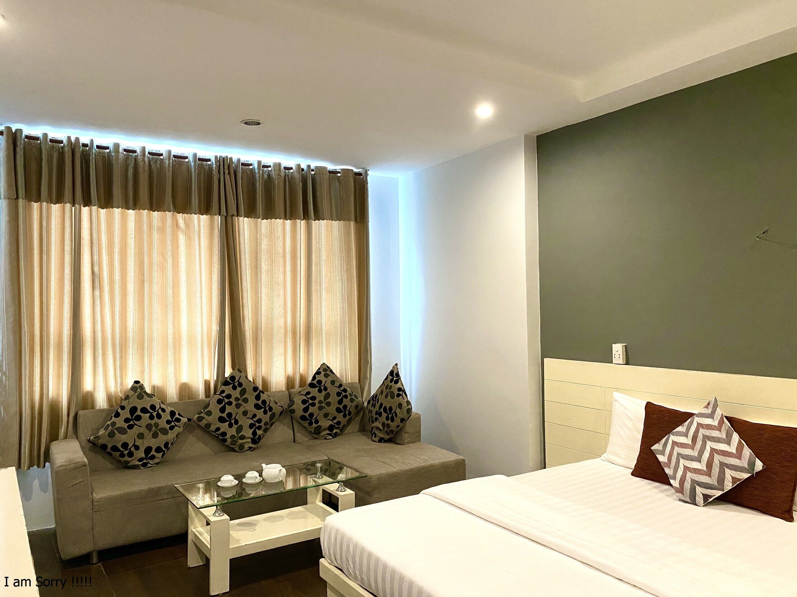 A modern bedroom with a bed, a glass coffee table, a sofa with patterned cushions, and a window with curtains.