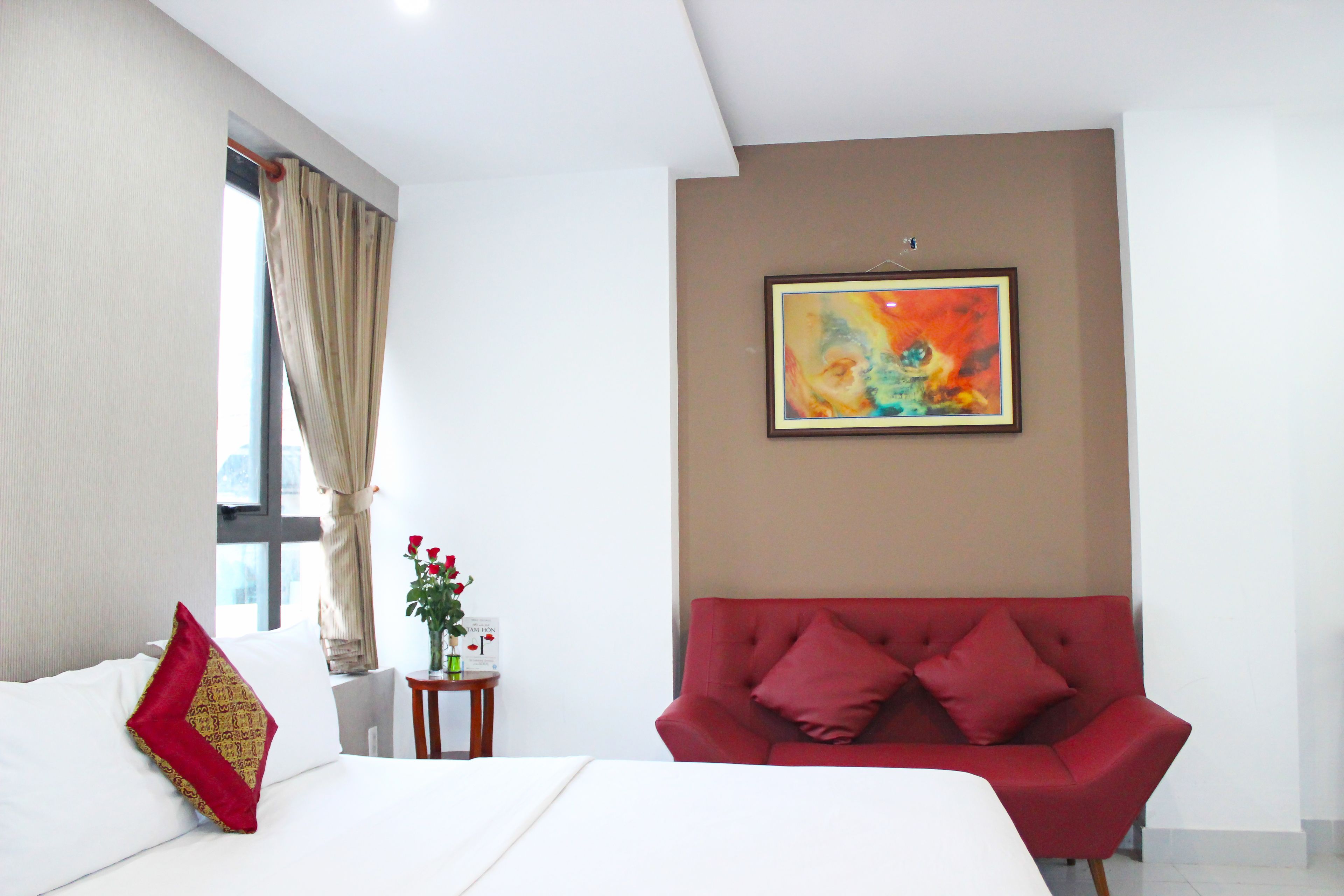 Ein Hotelzimmer mit einem Bett, einem roten Sofa, einem Gemälde an der Wand und einem Fenster mit Vorhängen.