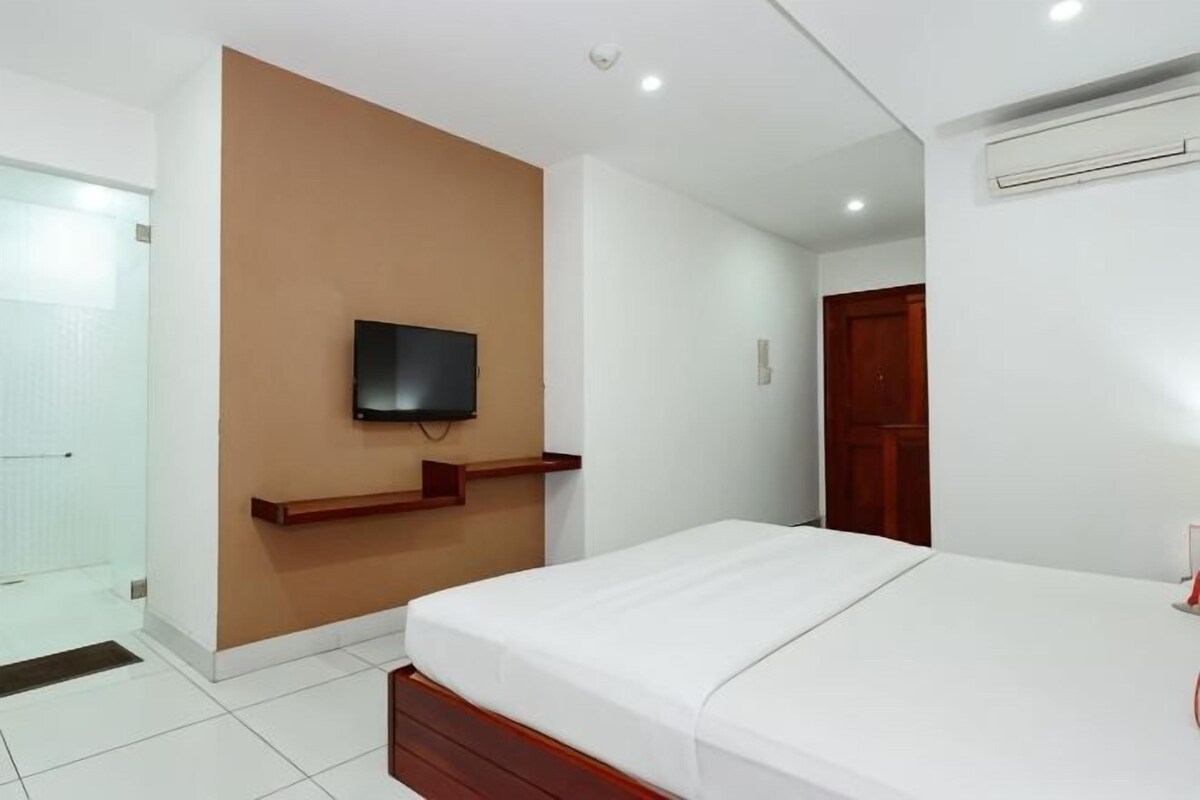 Habitación de hotel con cama, televisor montado, estante de madera, puerta y unidad de aire acondicionado.