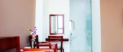 Habitación de hotel con comedor, baño con ducha de vidrio y cama.