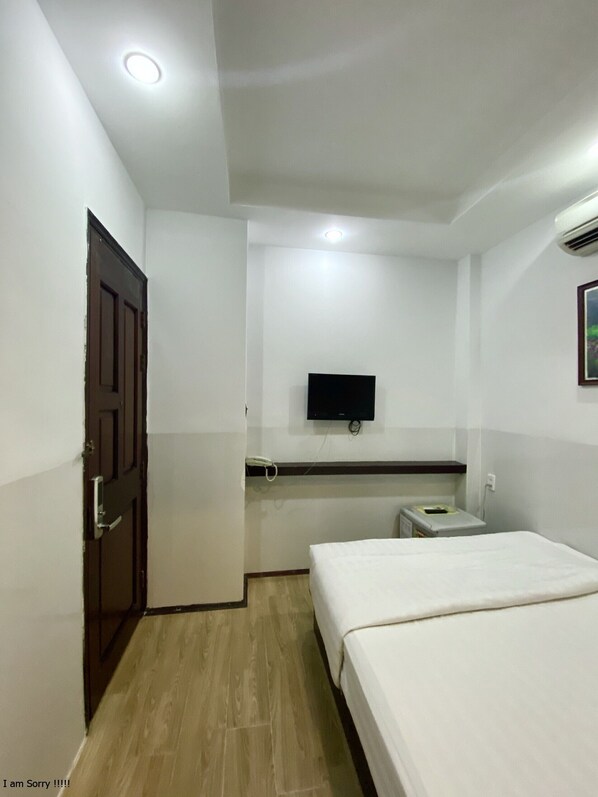 A hotel room with a bed, a television mounted on the wall, a bedside table, and a door.