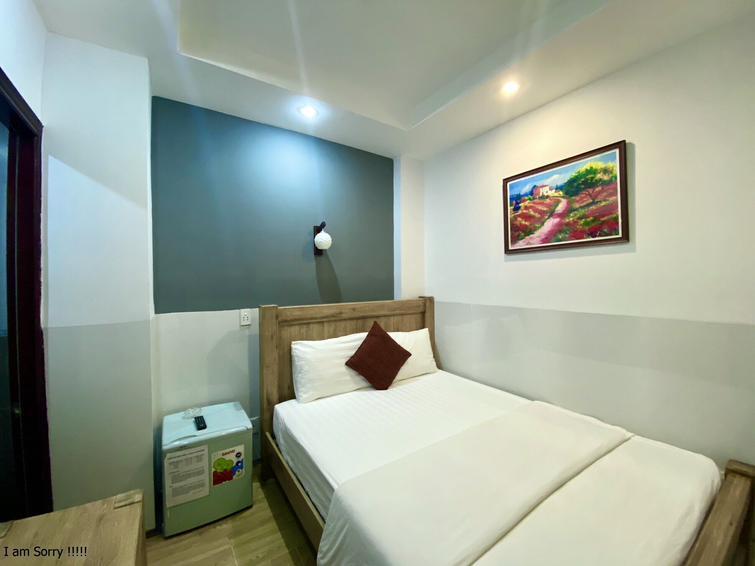 Une chambre d’hôtel avec un lit, une lampe fixée au mur, un tableau et un mini-bar.