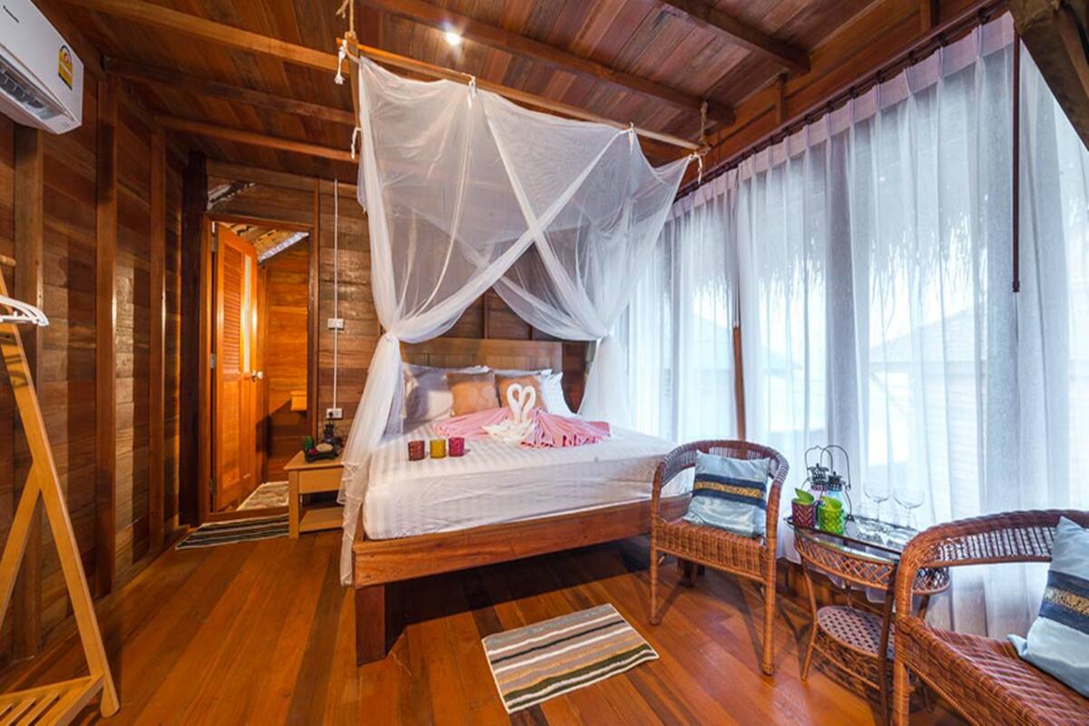 Quarto estilo cabana de madeira com cama de dossel, móveis de vime e vista para o exterior.
