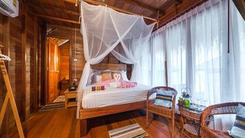 Un dormitorio de estilo cabaña con estructura de madera, cama con dosel, mobiliario de mimbre y vistas al exterior.
