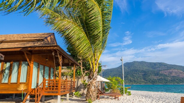 A wooden beach house with a balcony, a palm tree, and a view of the sea and mountains. - Lipe Beach Resort (Koh Lipe)
