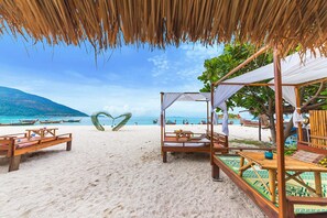 Une plage avec des chaises longues en bois et une structure surmontée d’un toit de chaume.