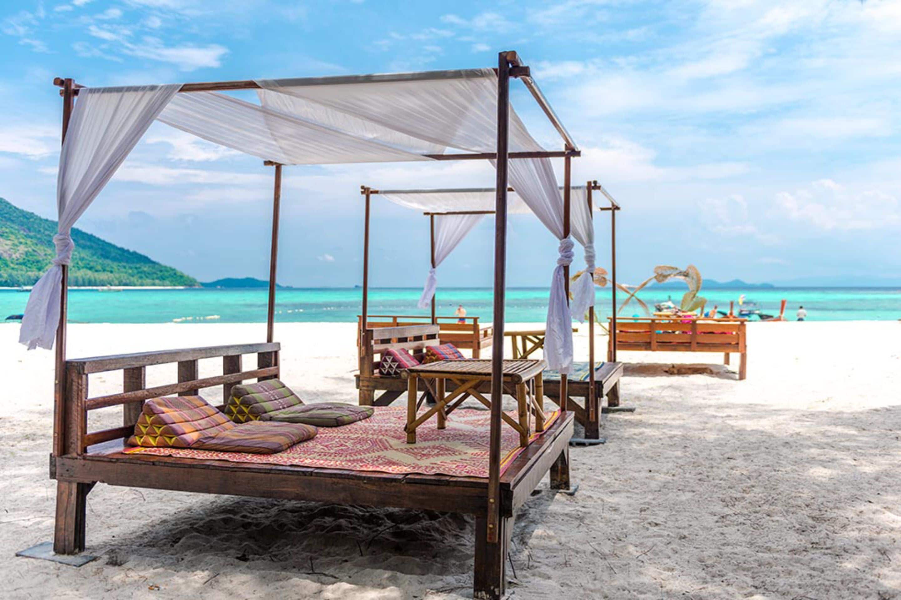 Una cama de playa con dosel, muebles de madera y vistas a la playa y al mar.